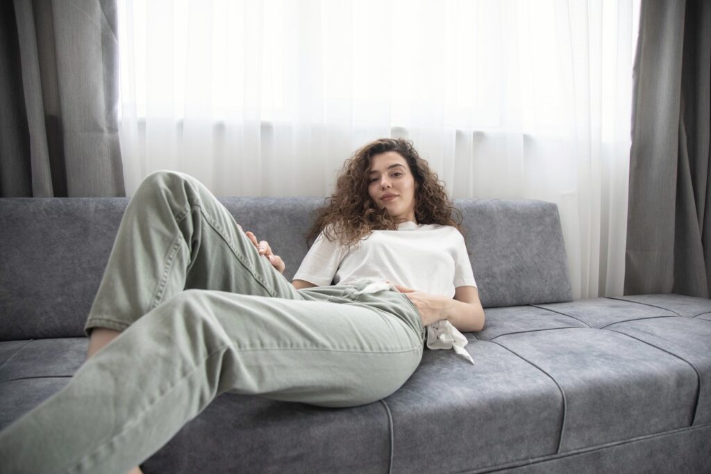 Kvinde hviler i sofaen ved et vindue med lyse gardiner