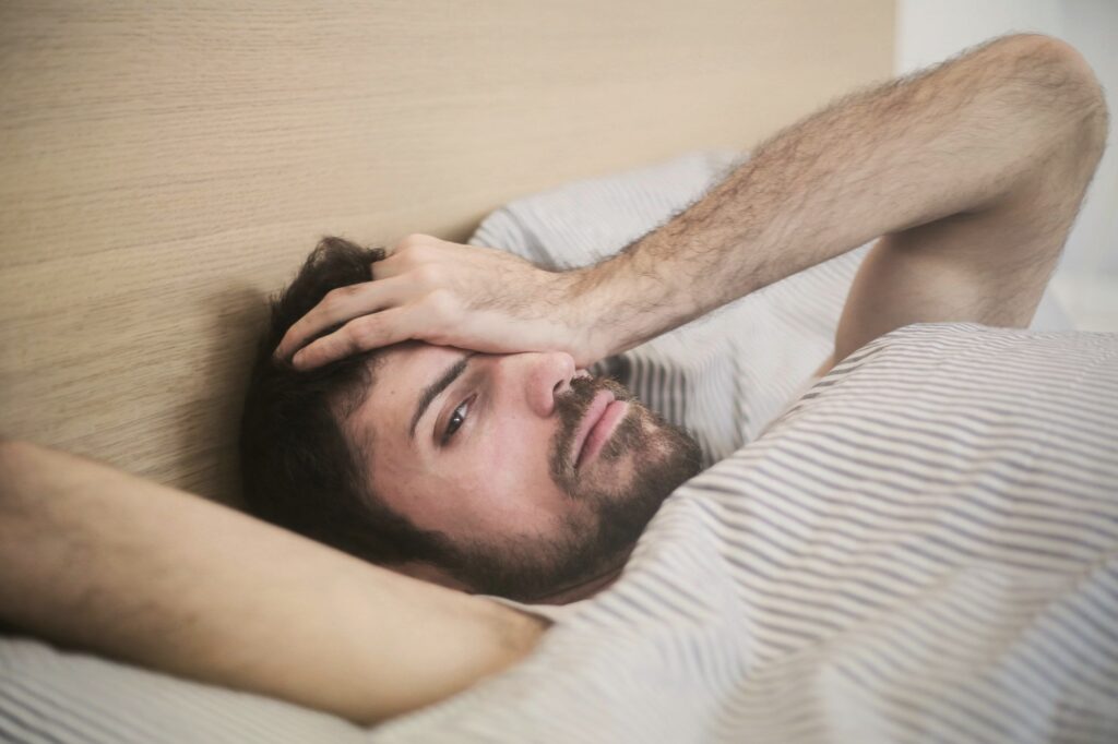 Mand ligger i sengen om morgenen med hånden mod panden